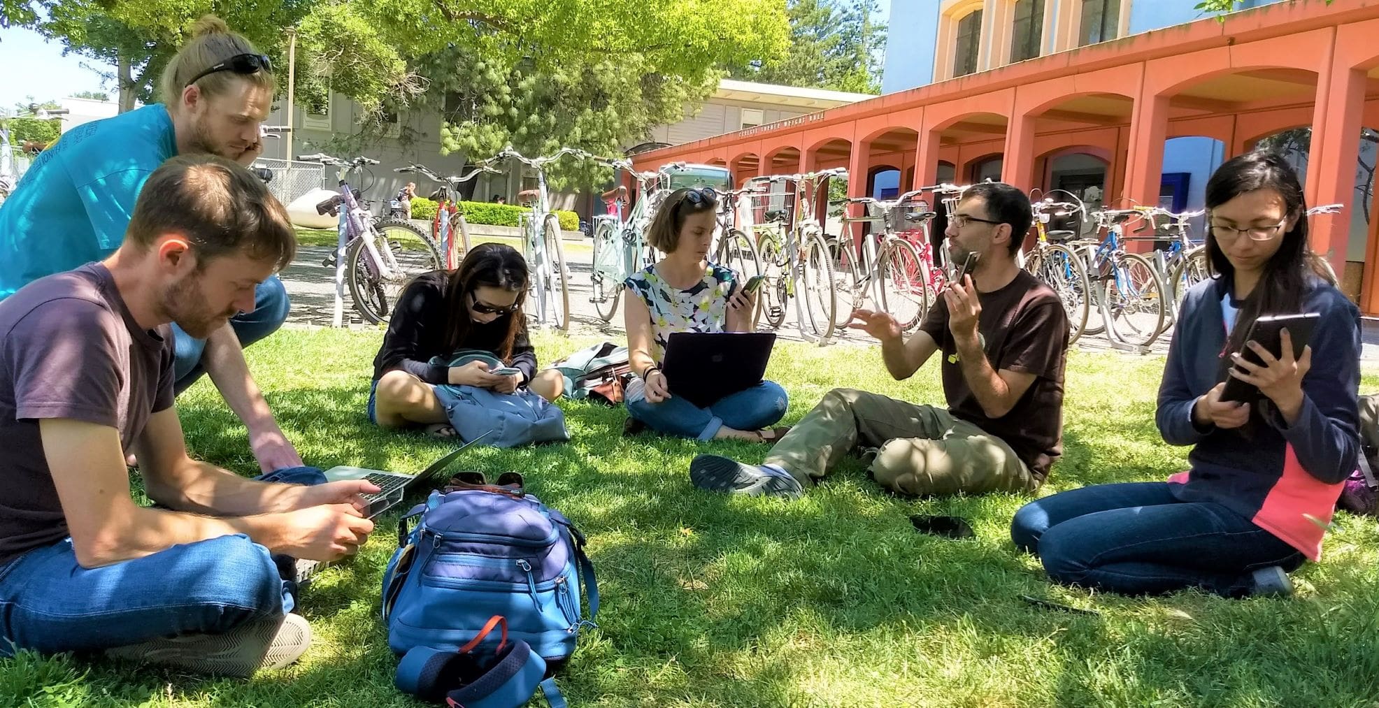 people sitting on grass learning to use mobile devices for field sampling